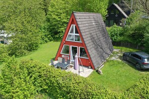 A red and white house with a slanted roof, surrounded by lush greenery. - Nur Dach Haus 12 (Kinding)