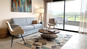 A modern living room with a light blue sofa, two armchairs, a coffee table with a laptop and a book, a lamp, and a large window with a view of greenery. - Appartement T3 de Standing - 2 Chambres 4/6 Personnes Porto Vecchio (Porto-Vecchio)