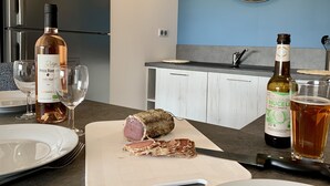 A kitchen with a cutting board, a knife, a bottle of wine, and a clock on the wall. - Appartement T3 de Standing - 2 Chambres 4/6 Personnes Porto Vecchio (Porto-Vecchio)