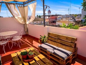 A rooftop terrace with a wooden bench, metal chairs, a small table, and potted plants. - Apartamento Romero (Sanlúcar de Barrameda)