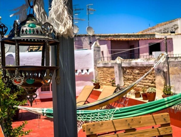 A hammock, a wooden bench, and a decorative lantern in an outdoor setting. - Apartamento Romero (Sanlúcar de Barrameda)