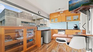 A modern kitchen with wooden cabinets, a built-in fridge, a dining area with a table and chairs, and a large window overlooking a cityscape.