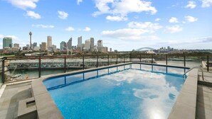 A rooftop pool with a city skyline view, including a bridge and high-rise buildings.