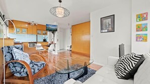 A modern living room with a glass coffee table, a sofa with patterned cushions, and a kitchen in the background.