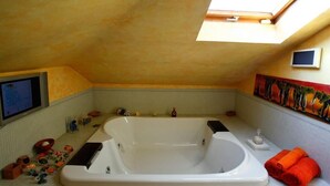 A bathroom with a large bathtub, a skylight, a small TV, and a colorful mural on the wall. - Casa Vacanza Diana (roma)