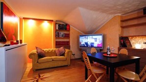A cozy living area with a yellow sofa, a dining table with chairs, a flat-screen TV, and a bookshelf. - Casa Vacanza Diana (roma)