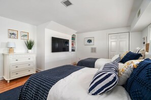 Een slaapkamer met twee bedden, een dressoir, een televisie en kunstwerken in lijsten aan de muur.