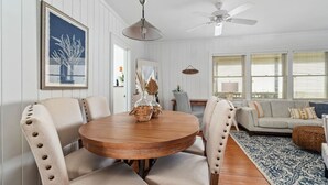 A dining area with a round wooden table, beige upholstered chairs, and a ceiling fan. - Classic Oceanfront Beach Cottage by Oceanana Pier (Atlantic Beach)