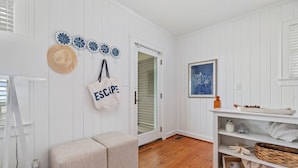 A room with white paneled walls, a wooden floor, a bench, a door, and a shelf with decorative items. - Classic Oceanfront Beach Cottage by Oceanana Pier (Atlantic Beach)