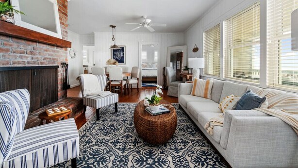 A spacious living room with a fireplace, a dining area, and a large window with blinds. - Classic Oceanfront Beach Cottage by Oceanana Pier (Atlantic Beach)