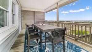 A covered outdoor patio with a wooden table and chairs, a blue patterned rug, and a view of the ocean. - Classic Oceanfront Beach Cottage by Oceanana Pier (Atlantic Beach)
