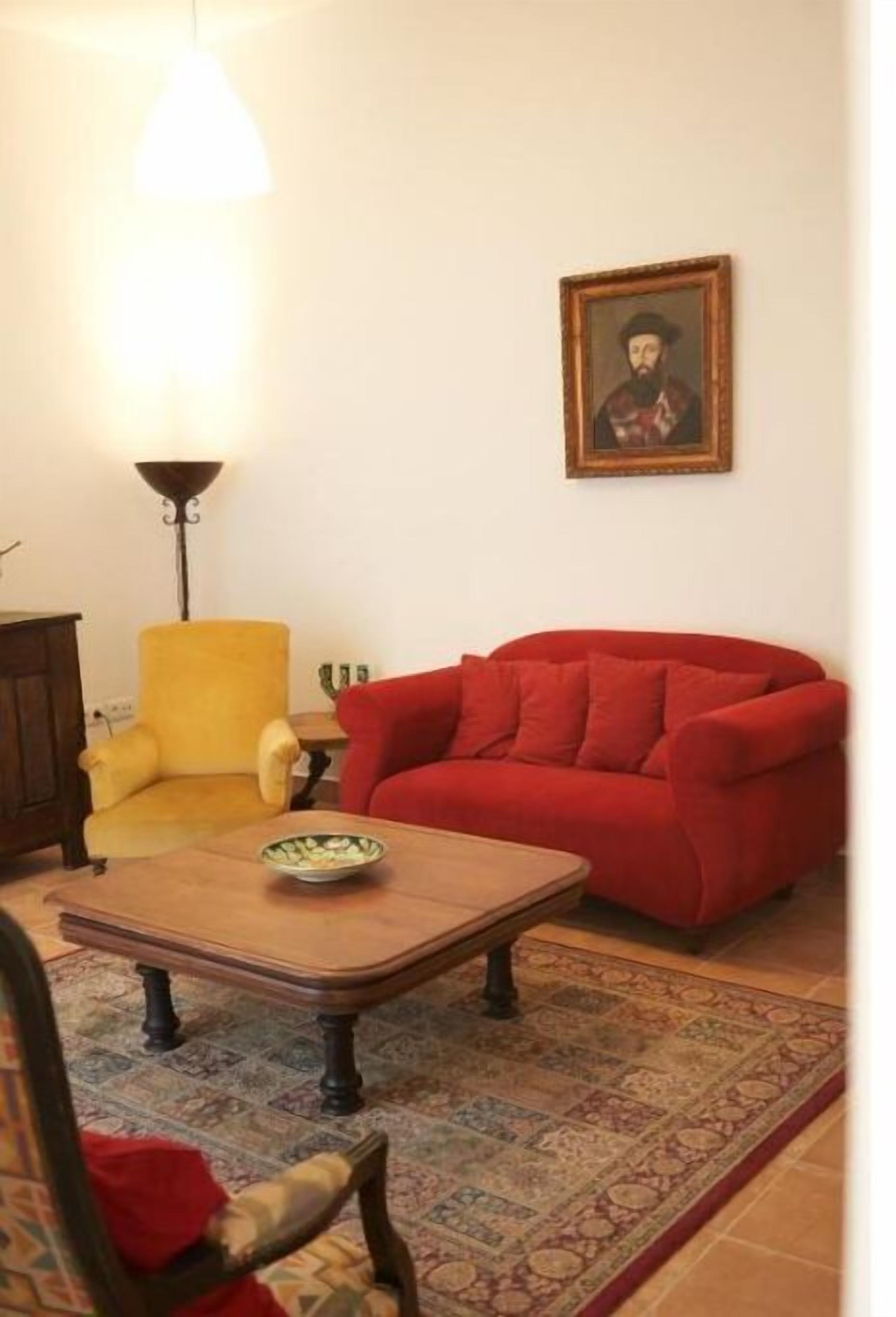 A living room with a red sofa, a yellow armchair, a wooden coffee table, and a patterned rug.