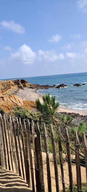 A beach with a wooden fence in the foreground, rocky coastline, and the ocean in the background.