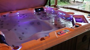 A hot tub with a control panel, surrounded by wooden panels and a window with a view of greenery.
