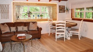 A cozy living room with a brown leather sofa, a wooden coffee table, and a dining area with white chairs and a wooden table.