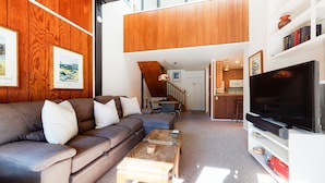 A living room with a brown sofa, a coffee table, and a TV. There is a staircase leading to a kitchen with wooden cabinets. - Summit 293 Bright, Spacious with Under Ground Parking, Walk to Eagle Lodge by RedAwning (Mammoth Lakes)