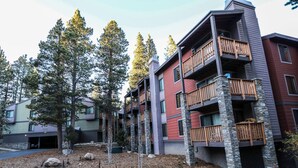 A multi-story building with balconies, surrounded by trees and a landscaped area with rocks and mulch. - Summit 293 Bright, Spacious with Under Ground Parking, Walk to Eagle Lodge by RedAwning (Mammoth Lakes)