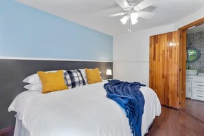 Ein Schlafzimmer mit einem Bett, einem Deckenventilator, einer Holztür und einem Nachttisch mit einer Lampe.