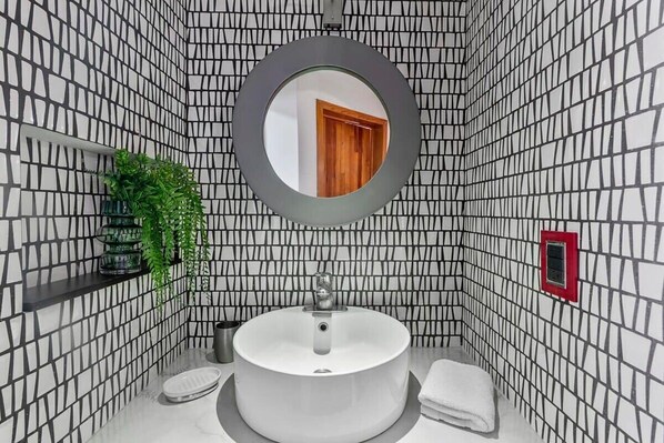 Un baño con un espejo redondo, un lavamanos y una planta en maceta.