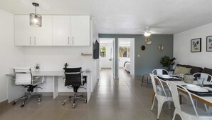Una cocina moderna con armarios blancos, un comedor con sillas blancas y un ventilador de techo.