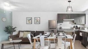 Una sala de estar moderna con comedor, un sofá, una mesa de centro y una cocina al fondo.