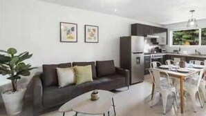 Una sala de estar moderna con un sofá, una mesa de comedor y sillas. Cuenta con una zona de cocina con un refrigerador y un microondas.