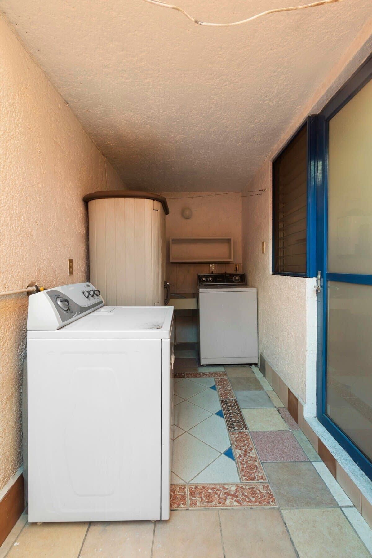 Un espace buanderie comprenant un lave-linge, un sèche-linge, un petit placard et une porte bleue.