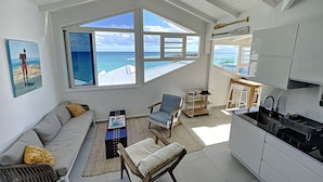 A spacious living area with a large window overlooking the ocean, a cozy seating arrangement, and a modern kitchen. - Deep Blue Vue mer et Piscine Privée (Le Gosier)