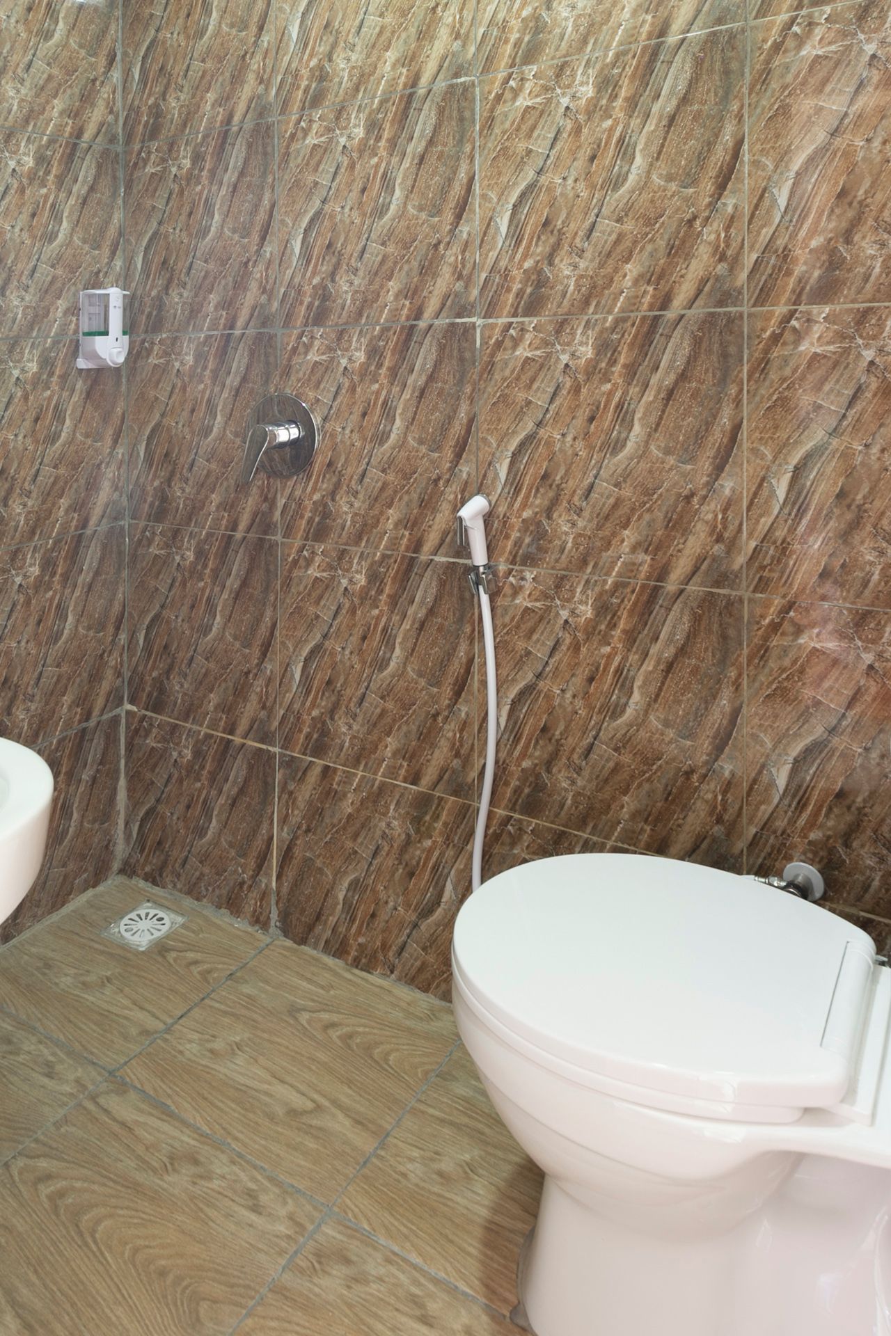 A bathroom with a marble wall, a toilet, and a shower.