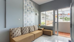 A modern living room with a sectional sofa, a patterned wall, and a sliding glass door leading to an outdoor area. - Oyo 3130 Valley (Lembang)