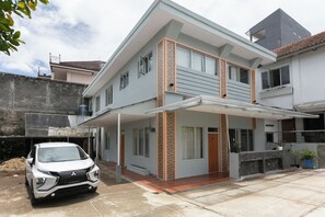 Uma casa moderna de dois andares com varanda coberta, um carro estacionado em frente e um pequeno jardim.