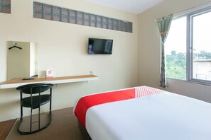 Une chambre d’hôtel comprenant un lit, un téléviseur fixé au mur, un bureau avec une chaise et une fenêtre avec des rideaux.