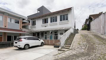 A two-story building with a car parked in front, a staircase leading to the entrance, and a paved pathway.