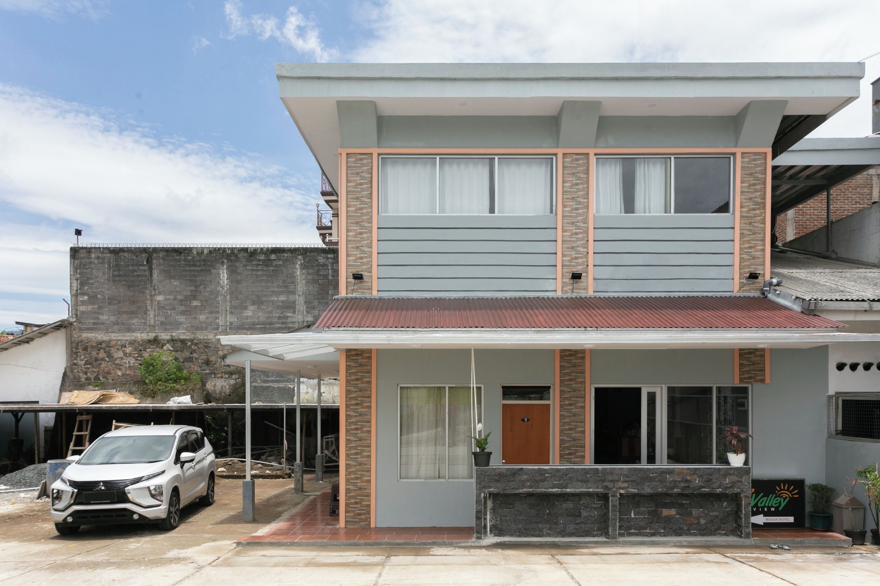 Una casa de dos pisos con balcón, cochera y entrada para vehículos.