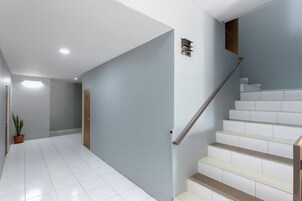 Un interior moderno con una escalera, suelo de baldosas blancas y una planta en maceta.