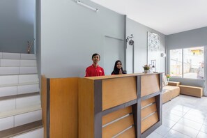 Un comptoir d’accueil au design moderne, un escalier recouvert de carreaux blancs et un espace détente offrant une vue sur l’extérieur.
