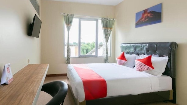 A hotel room with a bed, a desk, a chair, a TV mounted on the wall, and a window with curtains. - Oyo 3130 Valley (Lembang)