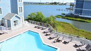 A pool area with lounge chairs and a view of a body of water. - Bayside & Beyond- 1st Floor Waterfront Condo with Pool, Gym & Boat Slip (Chincoteague)