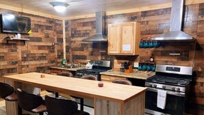 A kitchen with wooden walls, a wooden table, chairs, a stove, a sink, and cabinets.
