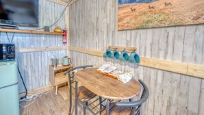 A rustic interior with a wooden dining table, a mounted television, and a painting of a mountainous landscape.