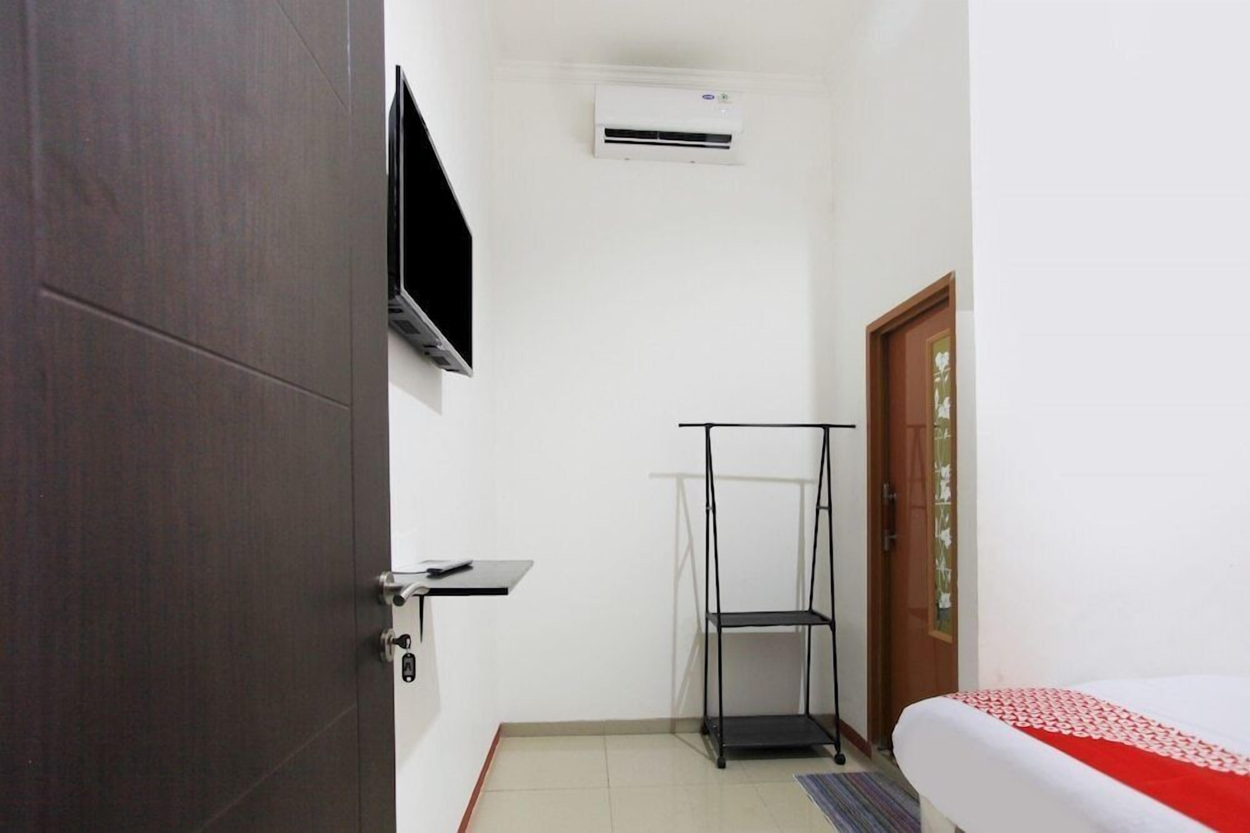 A small, clean room with a bed, a TV mounted on the wall, an air conditioning unit, and a wooden door.