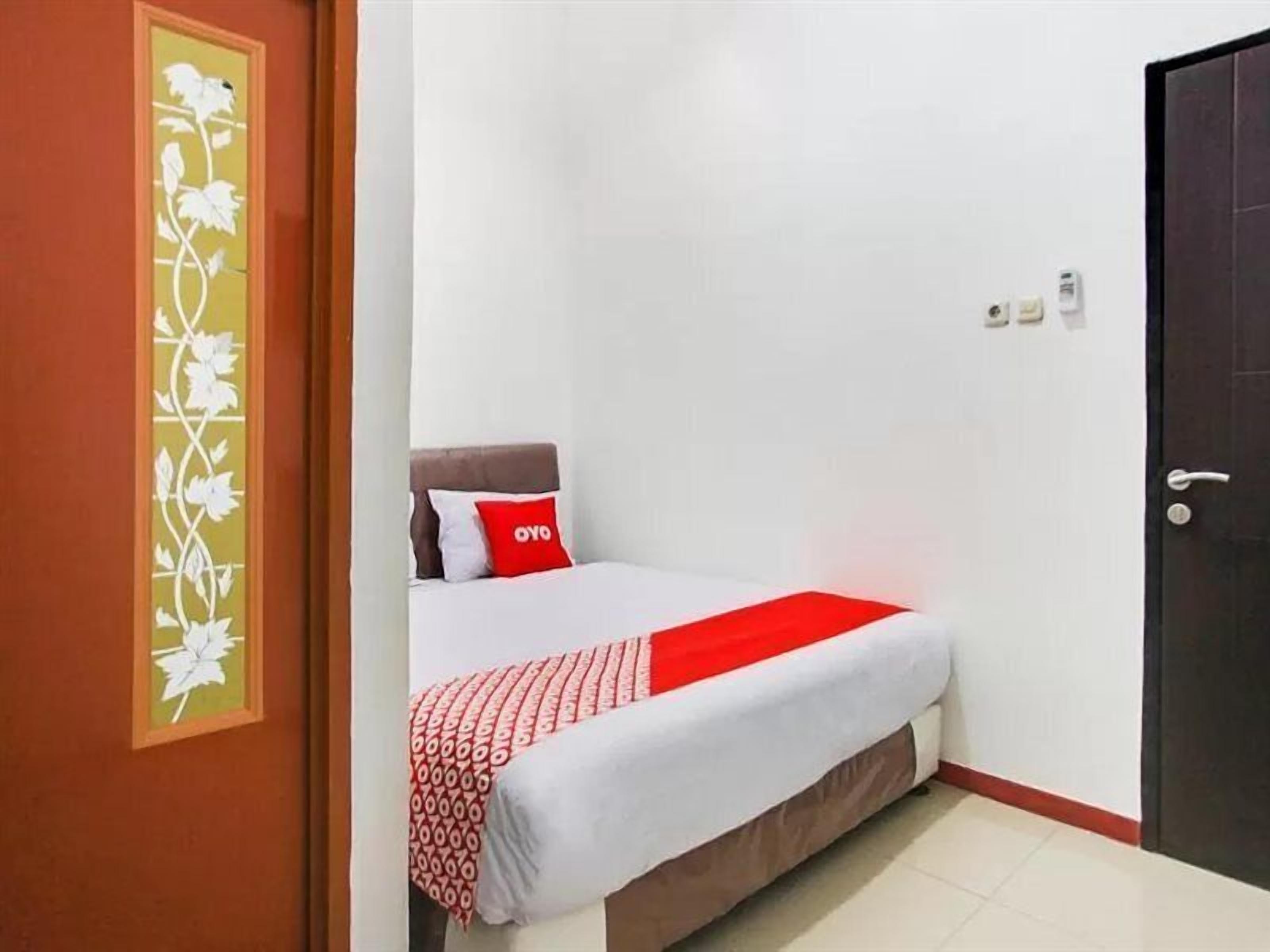 A bedroom with a bed, a red and white patterned blanket, a pillow with 'OYO' branding, and a door with a decorative panel.