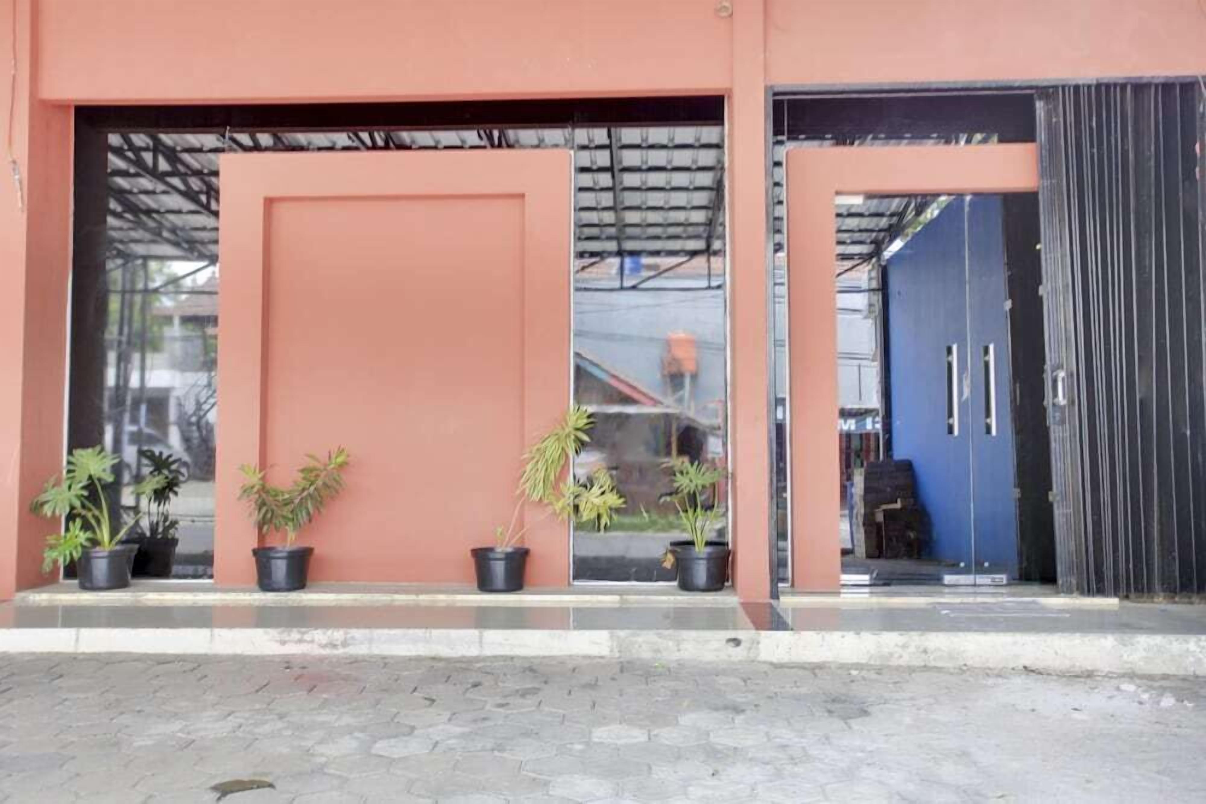 A building entrance with a large door and a smaller door, both with black frames. There are potted plants on the ground in front of the entrance.