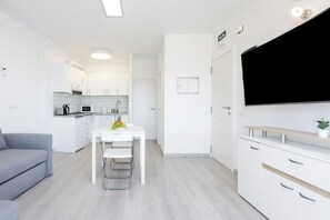 Una cocina moderna con armarios blancos, una mesa de comedor con sillas y un televisor de pantalla plana montado en la pared.