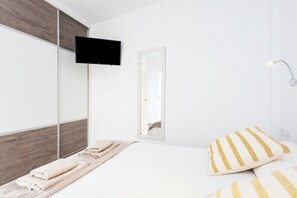 Un dormitorio moderno con una cama, un televisor montado en un panel de madera, un espejo y una lámpara de noche.