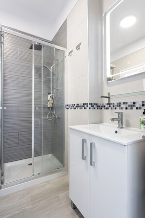 Un baño moderno con ducha envuelta en vidrio, un lavamanos blanco con un espejo encima y un salpicadero de azulejos.