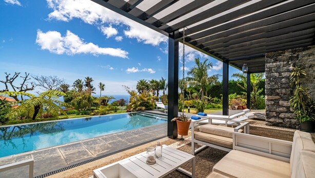 Ein Poolbereich mit Liegestühlen, einem Tisch und Blick auf den Ozean.