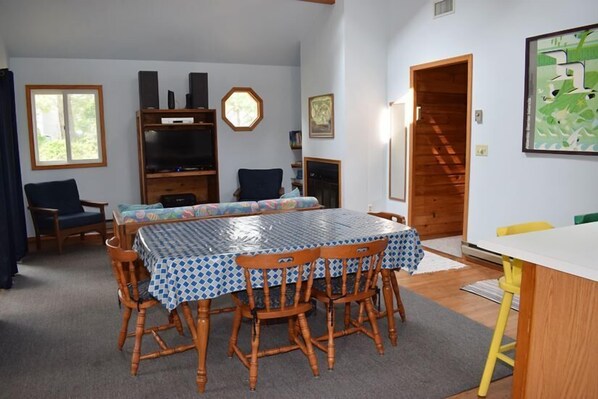 Uma área de refeições com uma mesa coberta por toalha quadriculada azul e branca, rodeada por cadeiras de madeira.