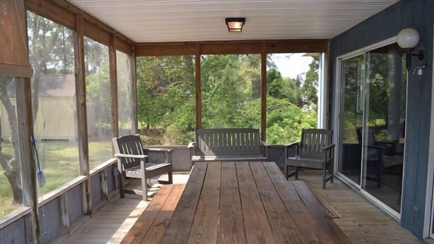 A covered patio with wooden flooring, a bench, and chairs.
