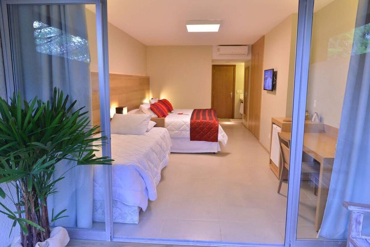 Une chambre d’hôtel avec deux lits, un bureau, une chaise, une plante en pot et un téléviseur fixé au mur.